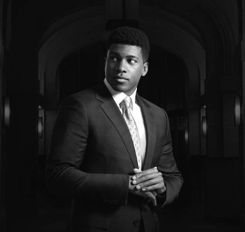 Eric Goree in a black suit in a black and white photo background.