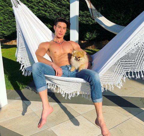 Justin Jedlica topless, wearing a jeans pant with pet in hand at his garden.