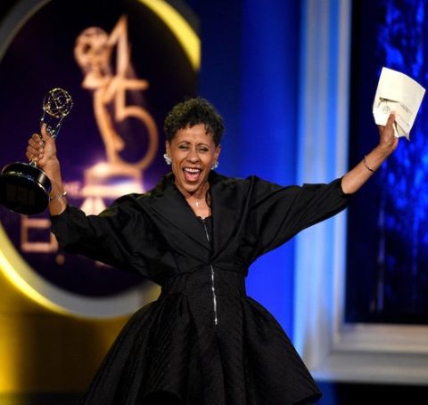 Vernee Watson-Johnson in a black dress celebrates on the stage with her Emmy award. 