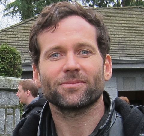 Eion Bailey looks at the camera, while wearing a black jacket. 