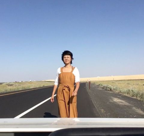 Charlyne Yi in a brown dress standing at the middle of a road.