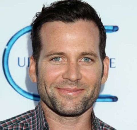 Eion Bailey in a red and white striped shirt looks at  the camera.