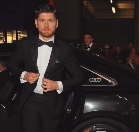 Kyle Soller in a black tux in front of a Mercedes.