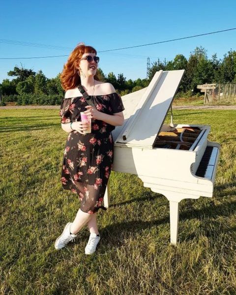Singer, Josie Charlwood giving a pose while standing next to the white piano.