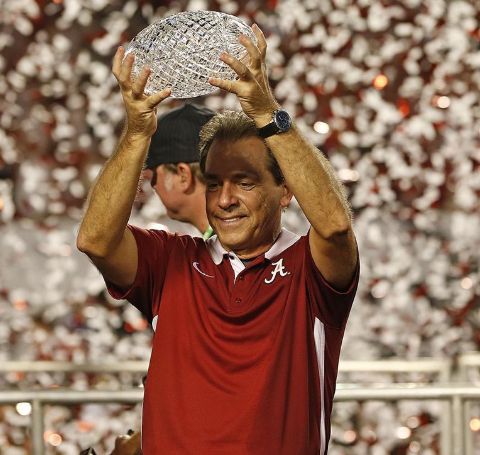 Nick Saban in a red t-shirt with a trophy on hand.