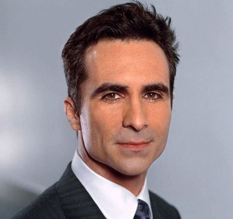 Nestor Carbonell in a black suit with black tie. 