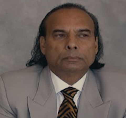 Bikram Choudhury in a grey suit and brown tie.