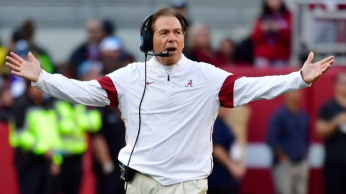 Nick Saban in a white jacket and headsets on ears.