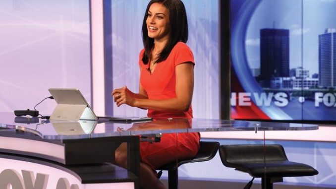 Shaina Humphries in a red dress reporting a news.