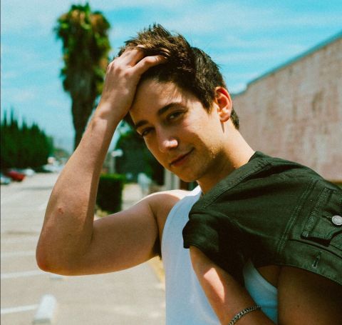 Milo Manheim in a white top poses for a picture.