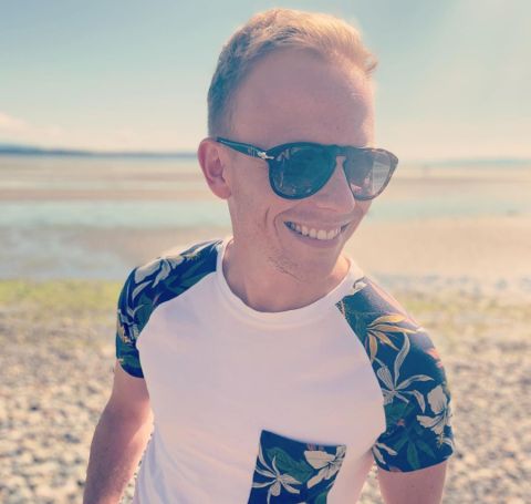 Adrian Petriw in a white t-shirt poses at a beach. 