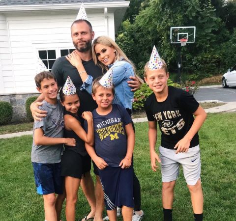 Jackie Goldschneider in blue poses alongside husband Evan Goldschneider and her four children.
