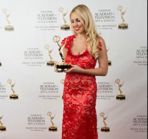 Jenn Barlow in a red dress poses with her Emmy Award.