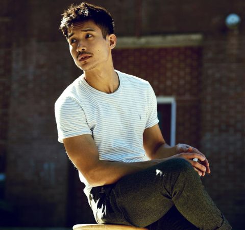 Manny Jacinto in white t-shirt poses for a photo.