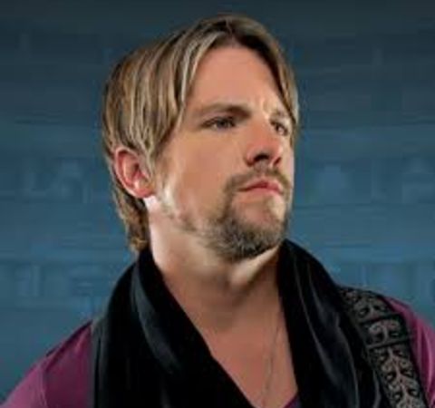 Zachary Knighton in a dark pink t-shirt poses for a picture.