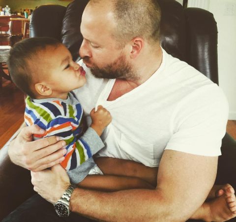 Ryen Russillo in a white t-shirt poses with a baby.