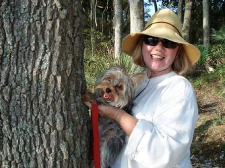 Judi Rolin holding her dog next to a tree