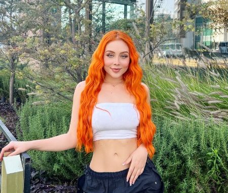 Maya Nazor with hair dyed orange on white top and black bottom.